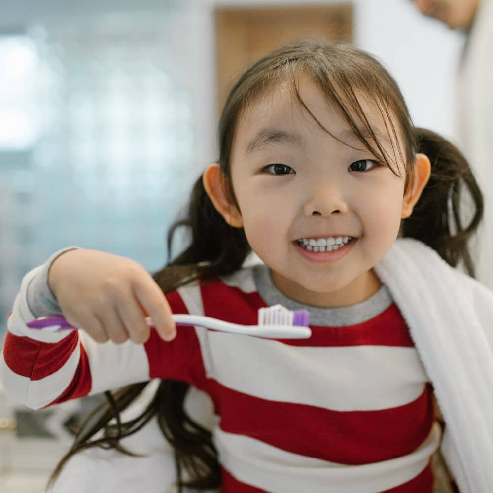 Young child smiling while showing her toothbrush with toothpaste.